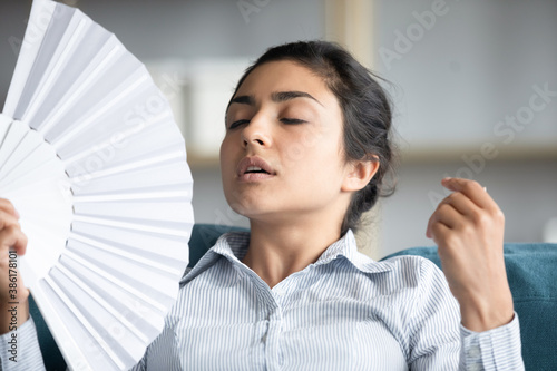 Tableau sur toile Close up image young indian ethnicity woman closed eyes lean on couch use white fan waver cooling herself feels overheated and annoyed with high temperature