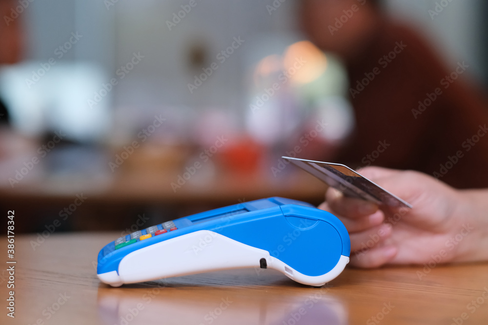 close up people holding credit card to pay over pos terminal on counter. blur background