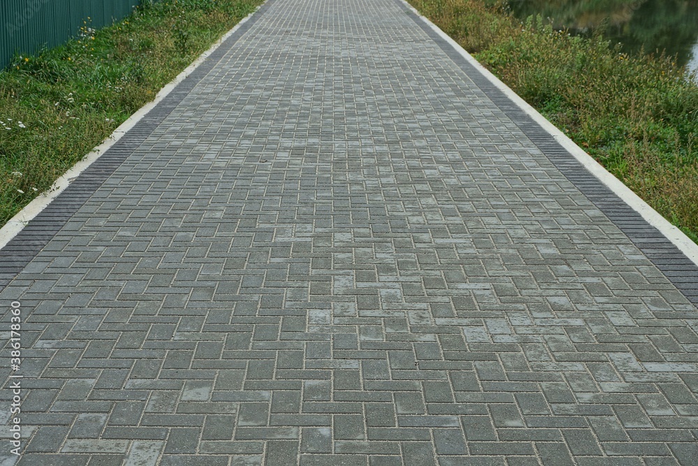 Obraz premium long alley of gray paving slabs along the green grass