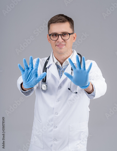Therapist wearing a pair of blue surgical gloves. Medic shows hands to the camera. Doctor in white scrubs and stethoscope on neck.