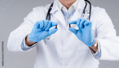 Portrait of a doctor`s hands showing two capsules between fingers. Selective focus. Medic in scrubs.