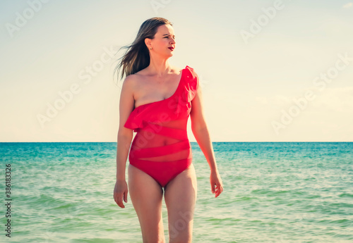 A young slender, beautiful European middle-aged woman flew to rest, mature pants in a red swimsuit against the sky. The wind develops her long dark hair