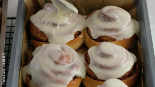 Pouring frosting on Freshly baked cinnamon rolls or Cinnabon close up. Sweet cream cheese frosting pouring on cinnamon rolls. Production of cinnamon rolls. Bakery products. Appetizing cinnamon buns