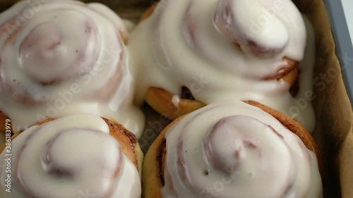 Pouring frosting on Freshly baked cinnamon rolls or Cinnabon close up. Sweet cream cheese frosting pouring on cinnamon rolls. Production of cinnamon rolls. Bakery products. Appetizing cinnamon buns