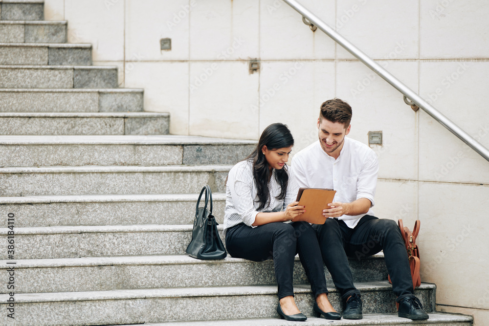 Young multi-ethnic business people sitting on steps and reading article on tablet computer