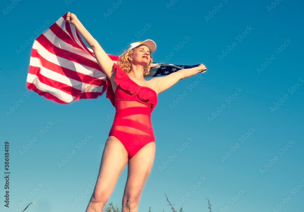 Beautiful cheerful blonde woman holding an American flag on the beach. A middle-aged woman in a red bikini is patriotically enthusiastic. Travel. USA flag. Copy space