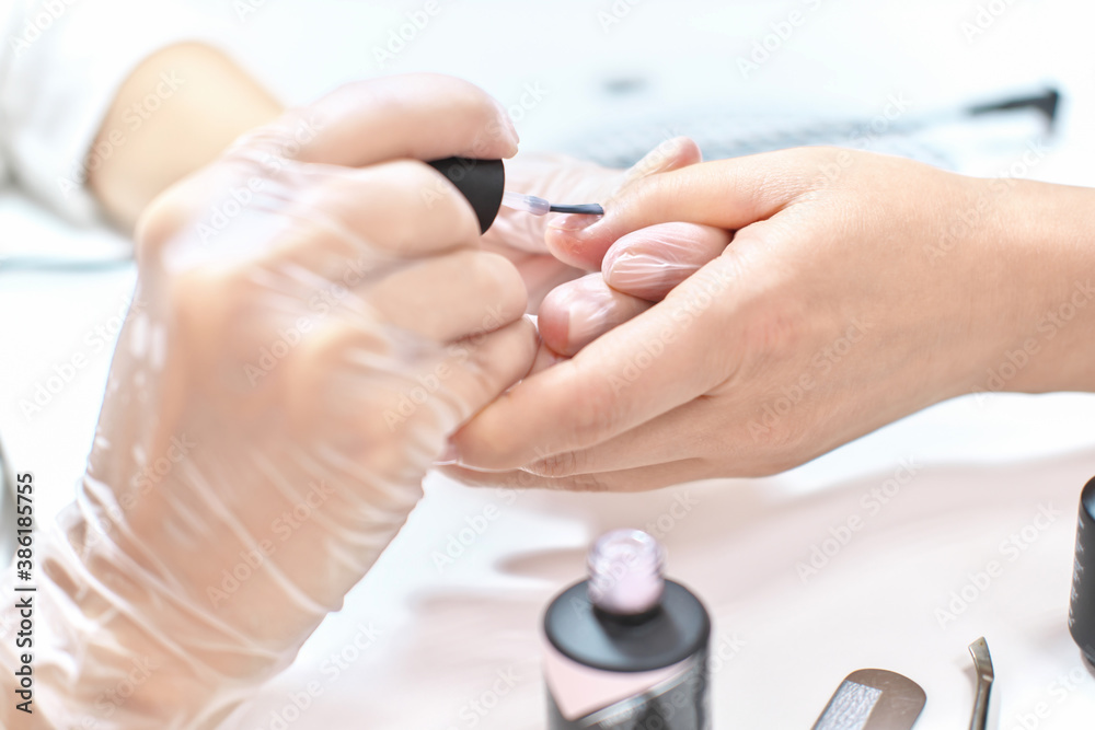 Fototapeta premium Beautician wearing protective gloves applying nail polish on client's hands. Manicure salon. Small business concept. 