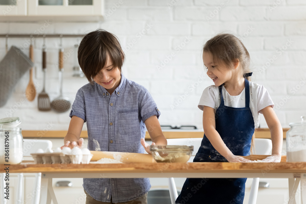 Two happy little kids siblings cooking together, rolling out dough, standing at wooden countertop in modern kitchen, cute preschool sister and brother preparing homemade pastry or pie for parents Two happy little kids siblings cooking together, rolling out dough, standing at wooden countertop in modern kitchen, cute preschool sister and brother preparing homemade pastry or pie for parents