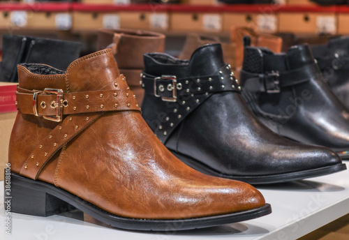 one pair of brown ankle boots. One pair of brown boots along with black ones lie in a row on a shelf, close-up side view.