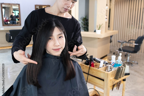 Hairdresser service customer in salon. Young Asian man LGBT design hairstyle for Asian woman in salon. Haircut and hair coloring concept.