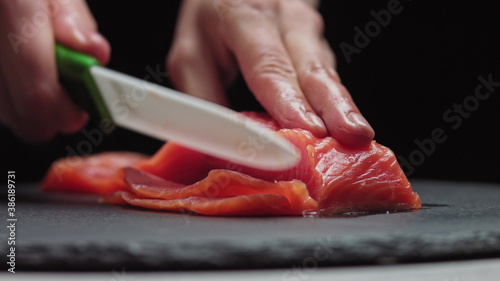 Sushi Chef Slices fresh Salmon on the sushi bar. Chef cutting salmon fillet at professional kitchen. Closeup chef hands slicing fresh fish slice in slow motion. Professional man cutting red fish