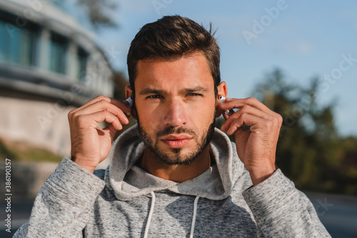 Portrait of a good-looking young male jogger putting earphones on before running