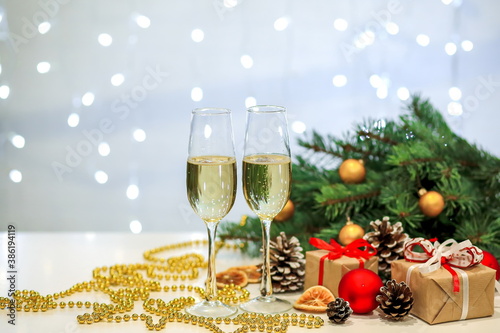 Two glasses of champagne composition with Christmas and new year decorations on a blurry background of burning garlands