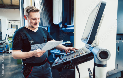 Worker in industrial workshop programming a cnc machine photo