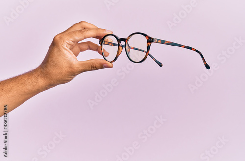 Hand of hispanic man holding glasses over isolated pink background.