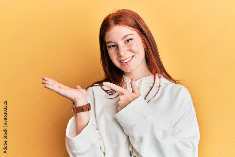 Young red head girl wearing casual sweatshirt amazed and smiling to the camera while presenting with hand and pointing with finger. Young red head girl wearing casual sweatshirt amazed and smiling to the camera while presenting with hand and pointing with finger.