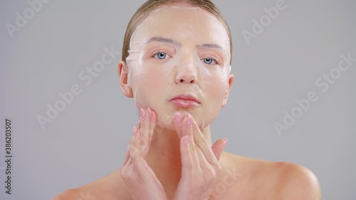 Close Up Beauty Portrait Of Young Caucasian Blonde Woman With Blue Eyes She Applying Finger White Paper Tissue Sheet Mask On Face On Gray Background Skin Care Concept Slow Motion