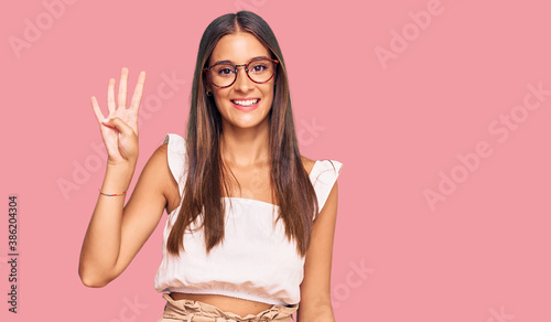 Young hispanic woman wearing casual clothes and glasses showing and pointing up with fingers number four while smiling confident and happy.