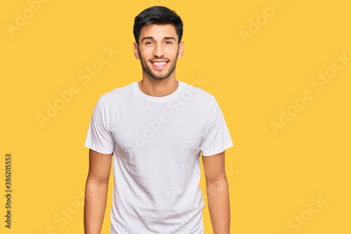 Young handsome man wearing casual white tshirt with a happy and cool smile on face. lucky person.