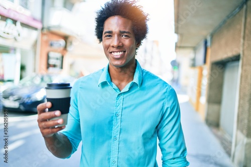 Young handsome african american man smiling happy. Standing with smile on face drinking cup of take away coffee walking at town street.