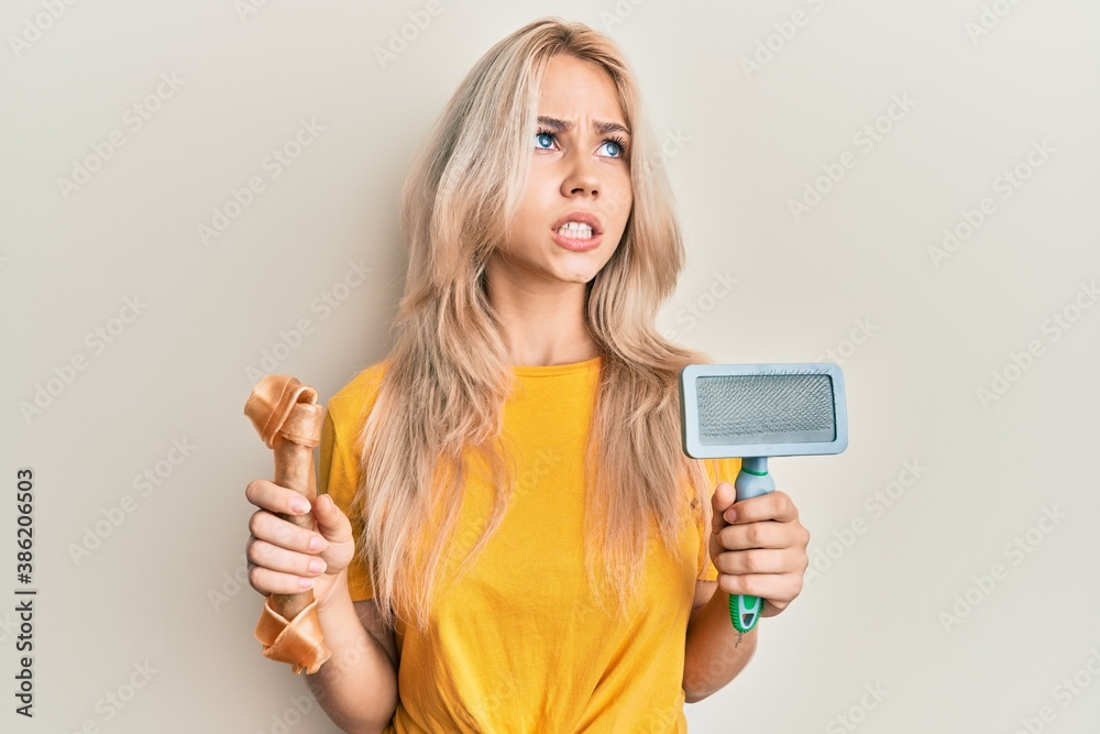 Beautiful caucasian blonde girl holding dog accesories angry and mad screaming frustrated and furious, shouting with anger looking up. Beautiful caucasian blonde girl holding dog accesories angry and mad screaming frustrated and furious, shouting with anger looking up.