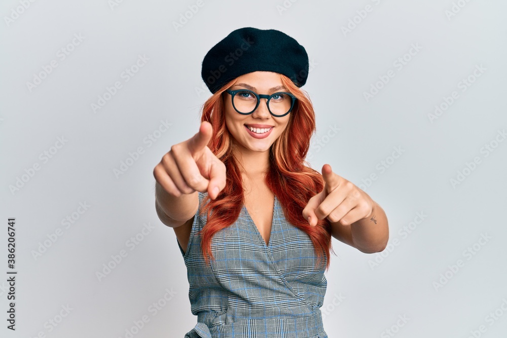Young redhead woman wearing fashion french look with beret pointing to you and the camera with fingers, smiling positive and cheerful Young redhead woman wearing fashion french look with beret pointing to you and the camera with fingers, smiling positive and cheerful