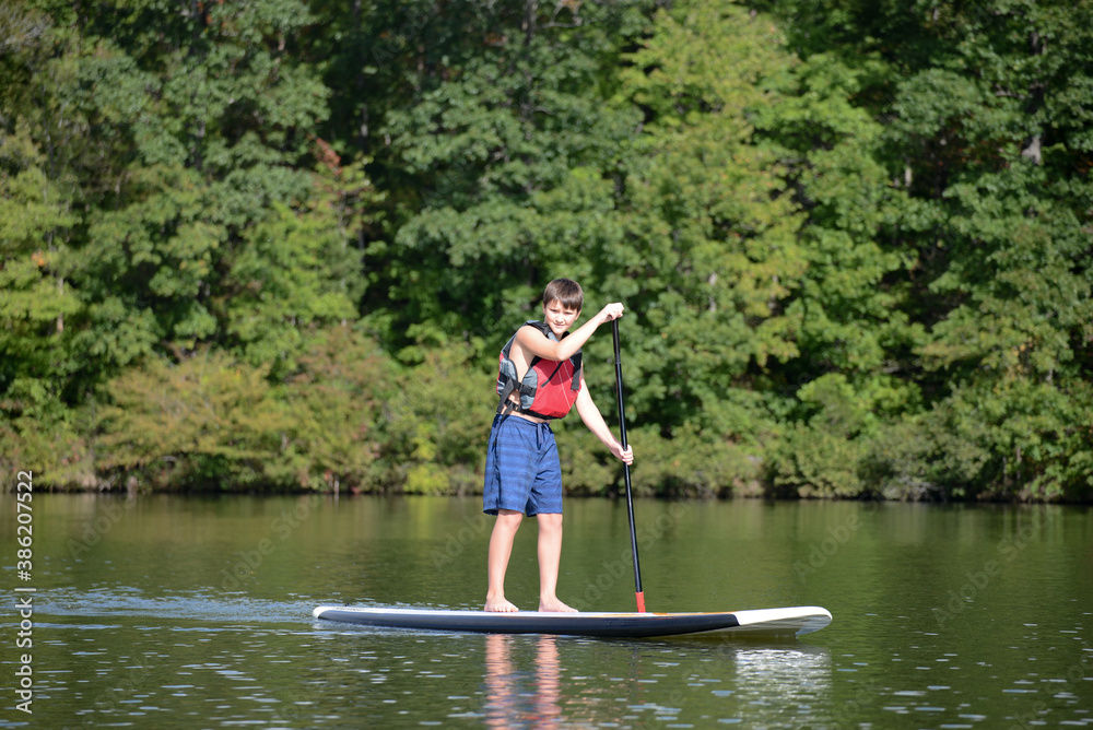 Boy standing up on a paddleboard on calm lake Boy standing up on a paddleboard on calm lake
