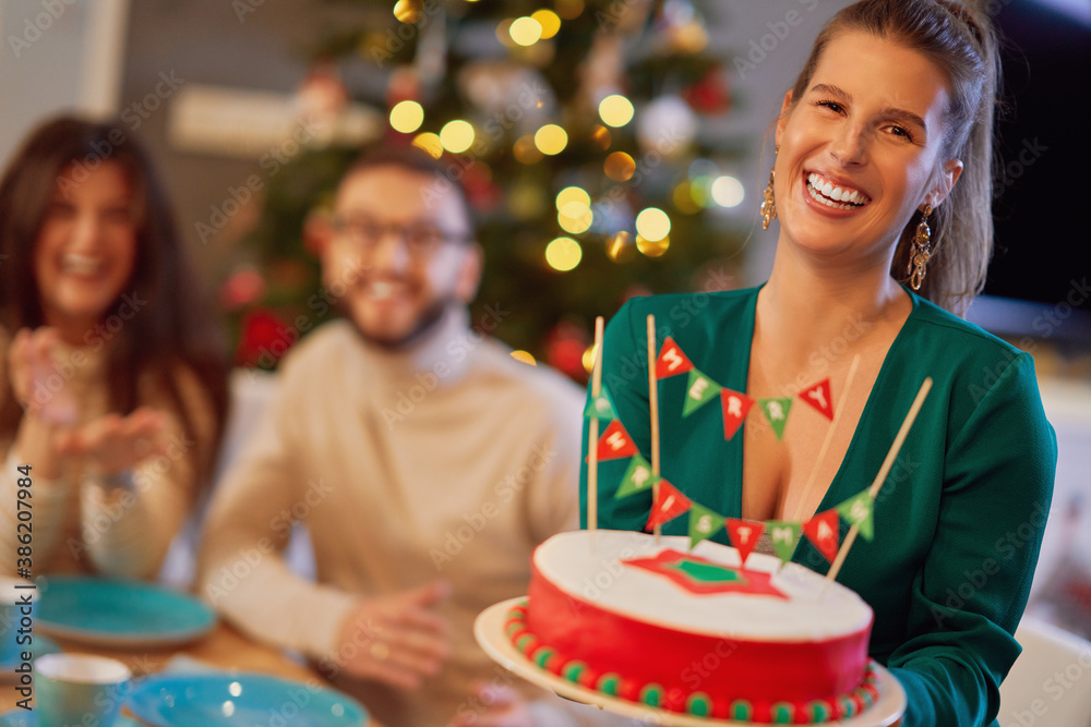 Fototapeta premium Group of friends celebrating Christmas at home with fancy cake