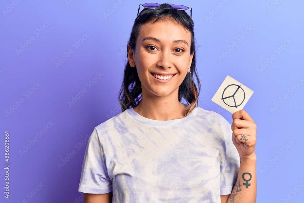 Young woman holding peace symbol reminder paper looking positive and happy standing and smiling with a confident smile showing teeth Young woman holding peace symbol reminder paper looking positive and happy standing and smiling with a confident smile showing teeth
