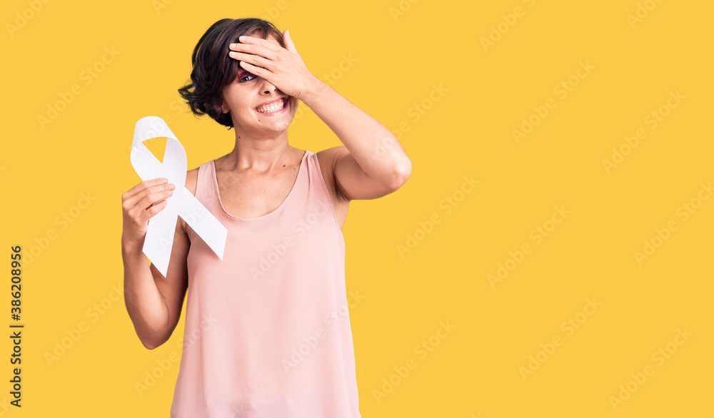 Beautiful young woman with short hair holding cancer awareness white ribbon stressed and frustrated with hand on head, surprised and angry face Beautiful young woman with short hair holding cancer awareness white ribbon stressed and frustrated with hand on head, surprised and angry face