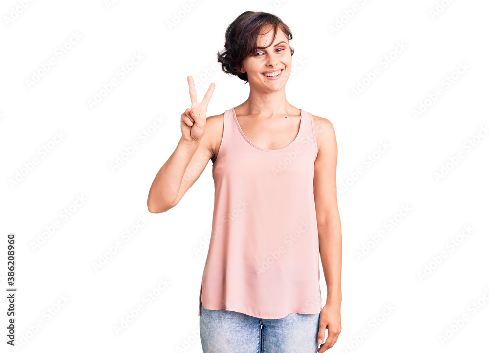 Beautiful young woman with short hair wearing casual style with sleeveless shirt showing and pointing up with fingers number two while smiling confident and happy. Beautiful young woman with short hair wearing casual style with sleeveless shirt showing and pointing up with fingers number two while smiling confident and happy.