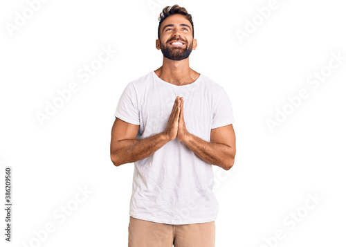 Young hispanic man wearing casual white tshirt begging and praying with hands together with hope expression on face very emotional and worried. begging.