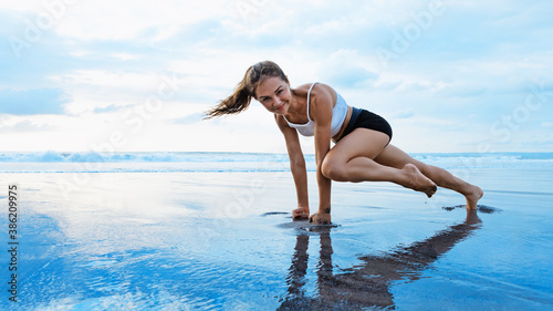 Sporty woman doing mountain climber exercise - run in plank to burn fat. Sunset beach, blue sky background. Healthy lifestyle at tropical island yoga retreat, outdoor activity, family summer vacation.