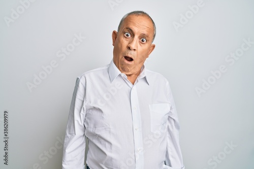 Handsome senior man wearing casual white shirt in shock face, looking skeptical and sarcastic, surprised with open mouth