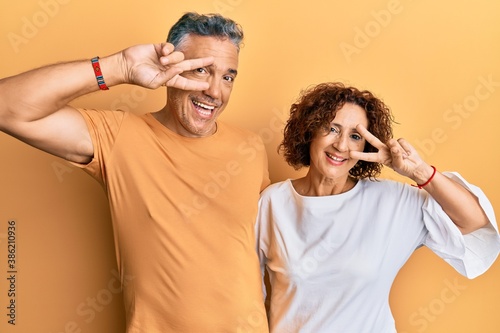 Beautiful middle age couple together wearing casual clothes doing peace symbol with fingers over face, smiling cheerful showing victory