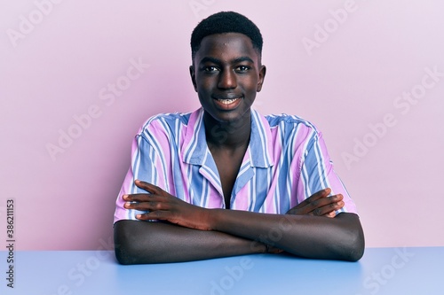 Young african american man wearing casual clothes sitting on the table happy face smiling with crossed arms looking at the camera. positive person.