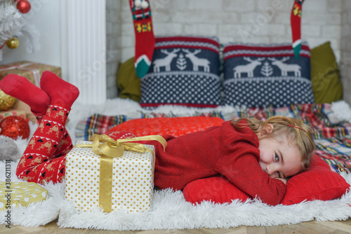 Cute little girl lying on the carpet. Christmas tree in the background. smiles. Beautiful little girl in the bright New Year's interior © MartaKlos