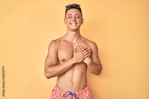 Young hispanic boy wearing swimwear shirtless smiling with hands on chest with closed eyes and grateful gesture on face. health concept.