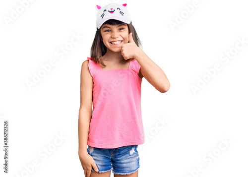 Young little girl with bang wearing funny kitty cap smiling happy and positive, thumb up doing excellent and approval sign