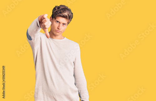 Young handsome man wearing casual clothes looking unhappy and angry showing rejection and negative with thumbs down gesture. bad expression.