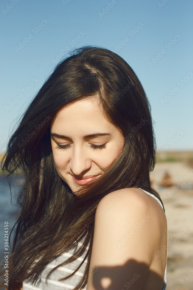 Summer girl portrait. Outdoors portrait of beautiful young brunette girl. Woman smiling happy on sunny summer or spring day outside by sea coast. Close-up portrait of a happy smiling woman.