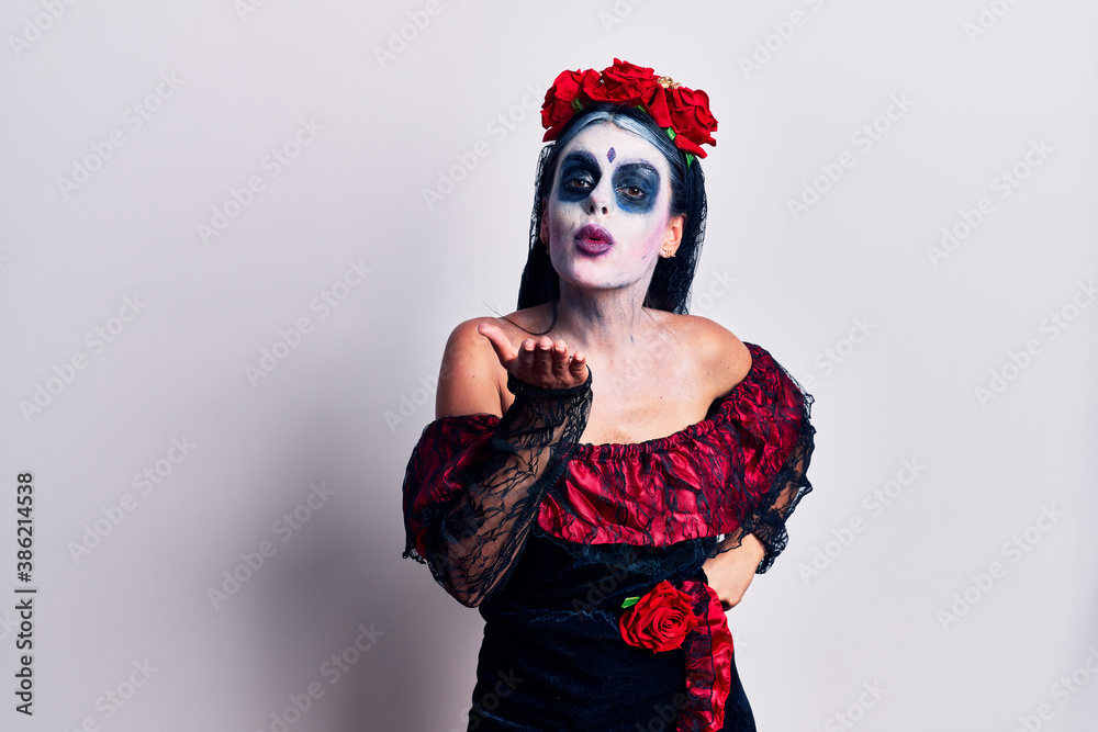 Young woman wearing mexican day of the dead makeup looking at the camera blowing a kiss with hand on air being lovely and sexy. love expression.