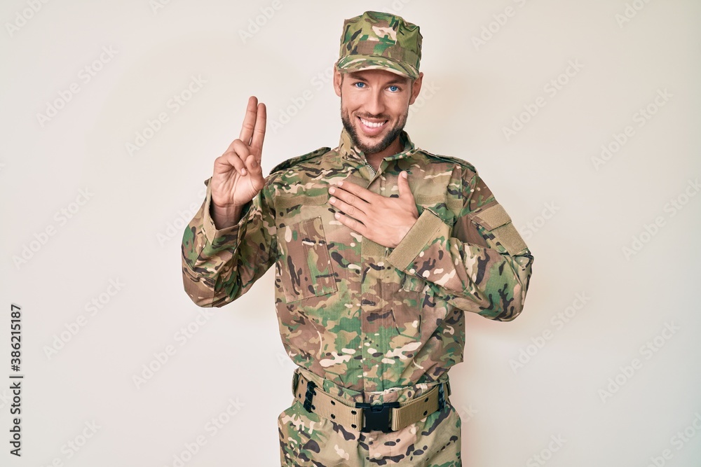 Young caucasian man wearing camouflage army uniform smiling swearing with hand on chest and fingers up, making a loyalty promise oath Young caucasian man wearing camouflage army uniform smiling swearing with hand on chest and fingers up, making a loyalty promise oath