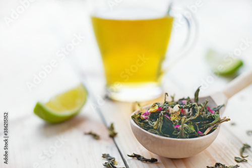 green tea leaves in wooden spoon with lime slices and mug of brewed tea on wooden background