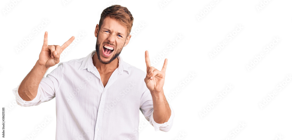 Young caucasian man wearing casual clothes shouting with crazy expression doing rock symbol with hands up. music star. heavy concept. Young caucasian man wearing casual clothes shouting with crazy expression doing rock symbol with hands up. music star. heavy concept.