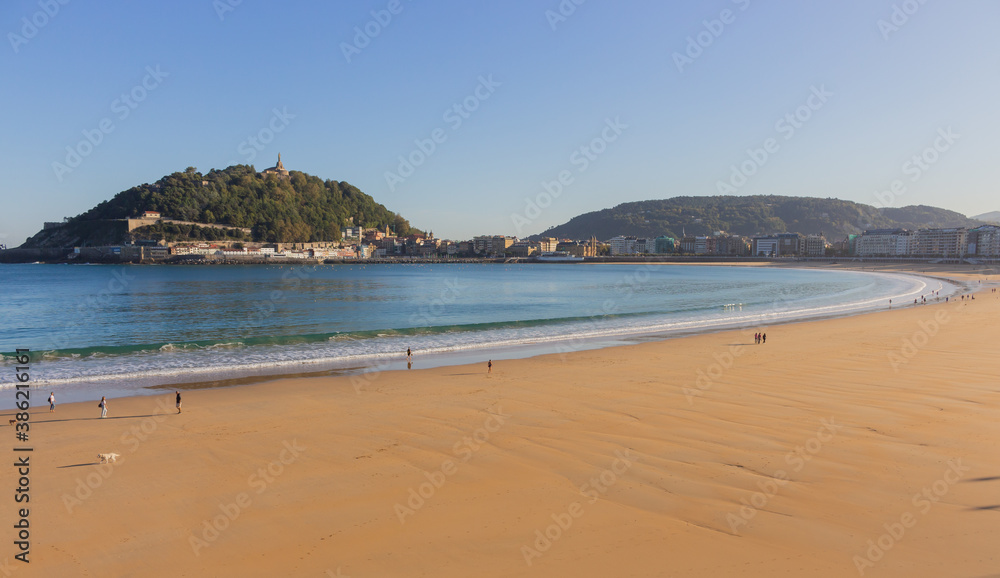 People walking with dogs on the beach called La Concha. Tourists in bay of Biscay in San Sebastian in autumn. Wide aerial beach in morning sunlight. Healthy and relax lifestyle. San Sebastian landmark