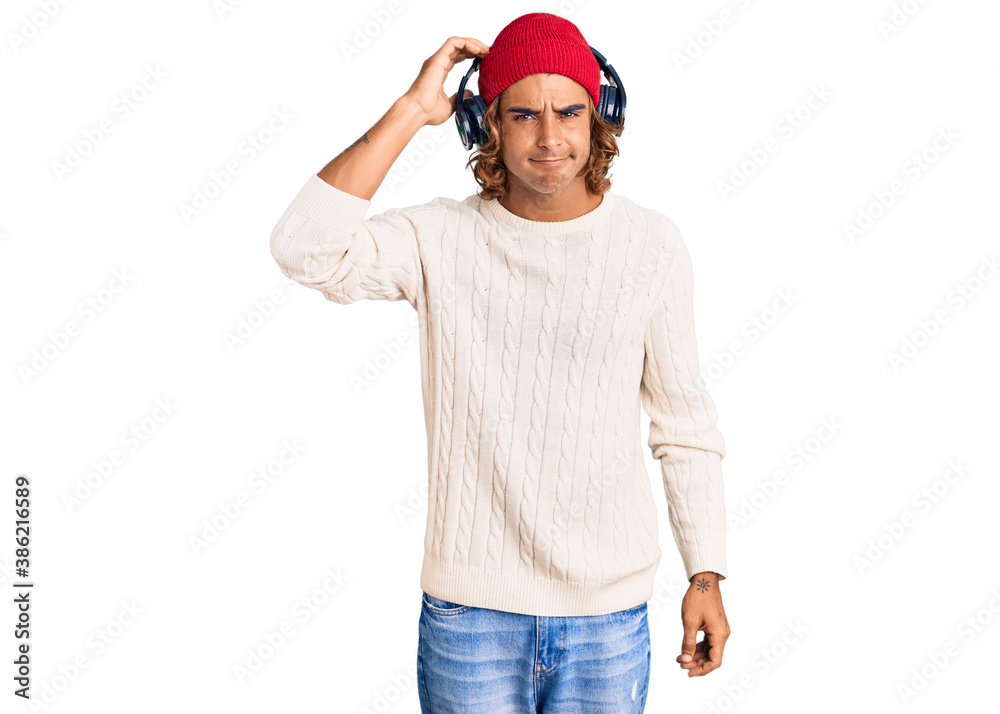 Naklejka premium Young hispanic man listening to music using headphones confuse and wonder about question. uncertain with doubt, thinking with hand on head. pensive concept.