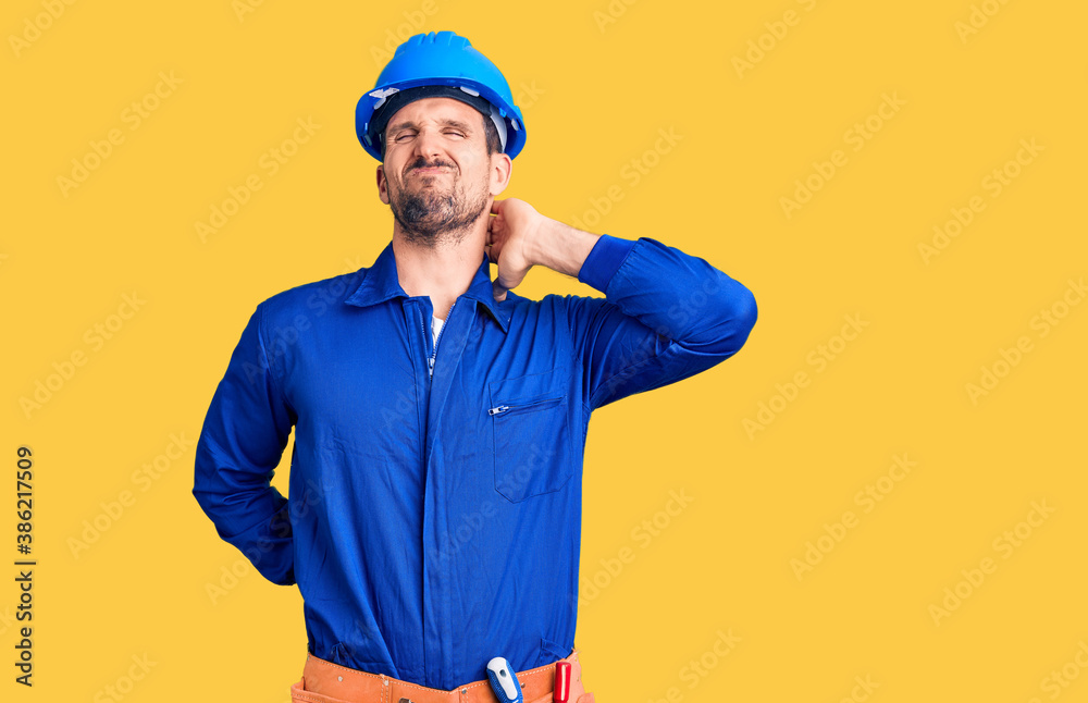 Young handsome man wearing worker uniform and hardhat suffering pain on hands and fingers, arthritis inflammation