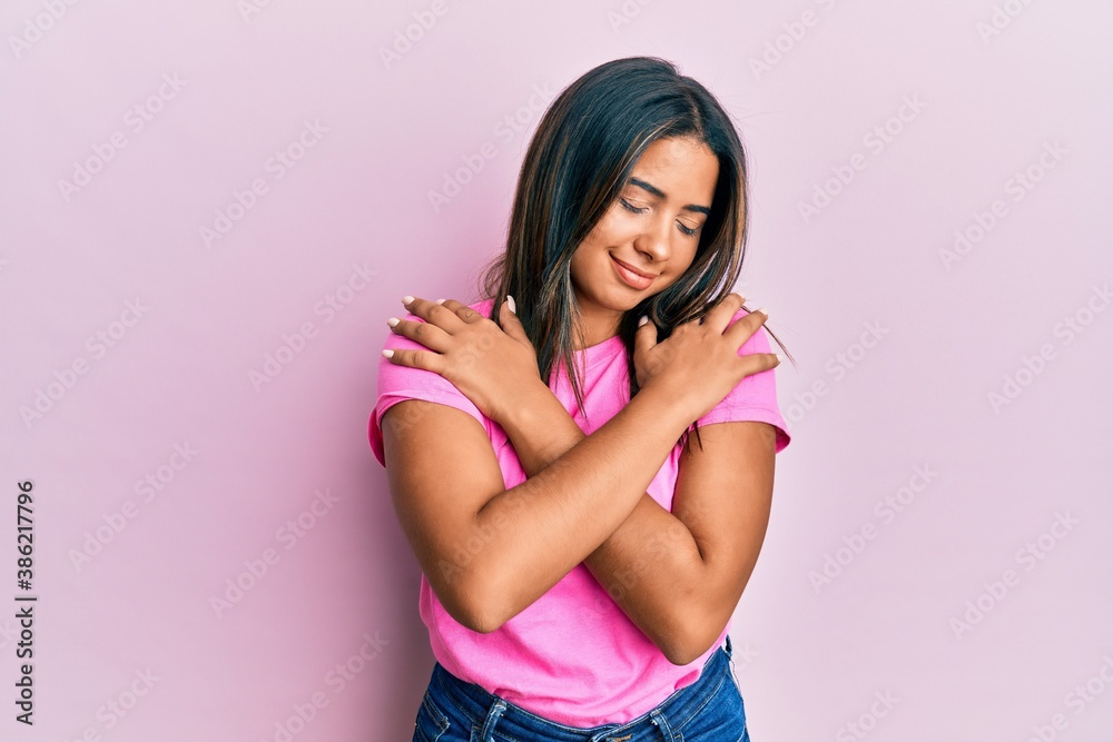 Young latin girl wearing casual clothes hugging oneself happy and positive, smiling confident. self love and self care Young latin girl wearing casual clothes hugging oneself happy and positive, smiling confident. self love and self care