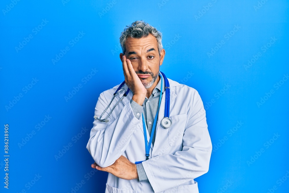 Middle age grey-haired man wearing doctor uniform and stethoscope thinking looking tired and bored with depression problems with crossed arms. Middle age grey-haired man wearing doctor uniform and stethoscope thinking looking tired and bored with depression problems with crossed arms.